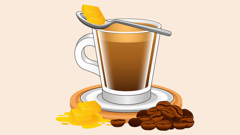 Glass of coffee with a spoon holding butter above it, next to melting butter and coffee beans.