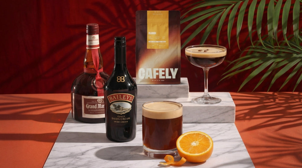 Coffee cocktails with Baileys and Grand Marnier beside a Cafely Hanoi coffee bag, with an orange garnish and palm leaf backdrop.