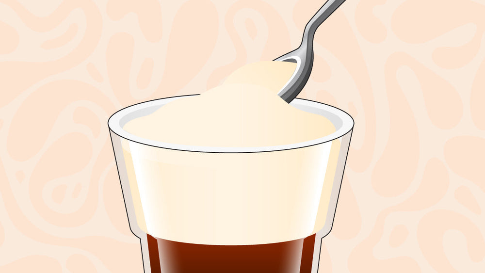 Spoon scooping creamy foam from the top of a glass of coffee.