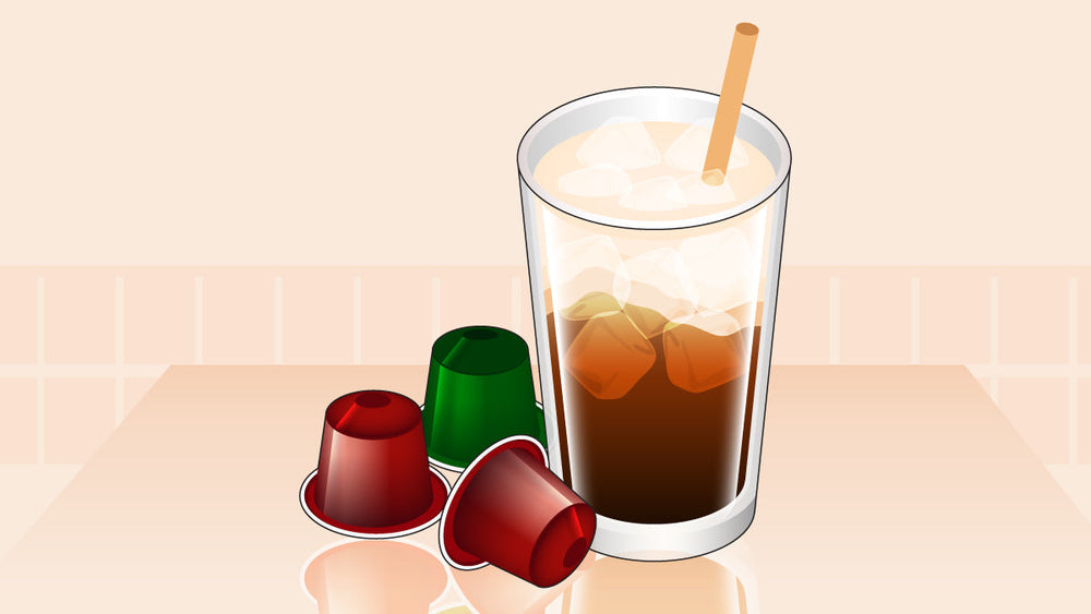 Glass of iced coffee with a straw beside three Nespresso-style coffee pods.